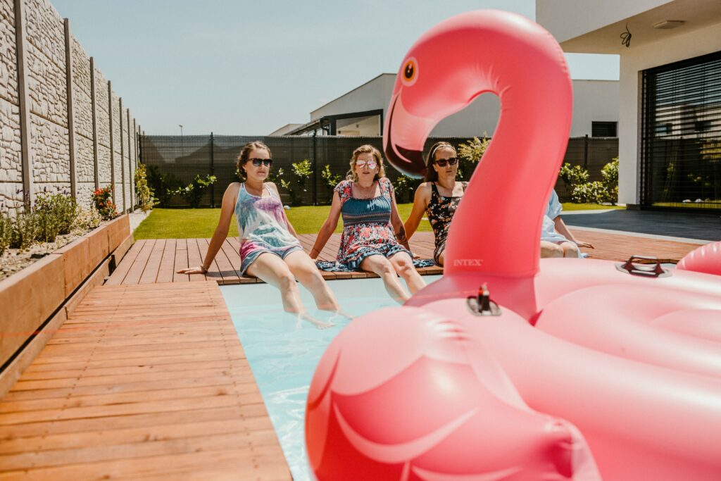 Women enjoying a sunny day by the pool with an inflatable flamingo, epitomizing summer fun.