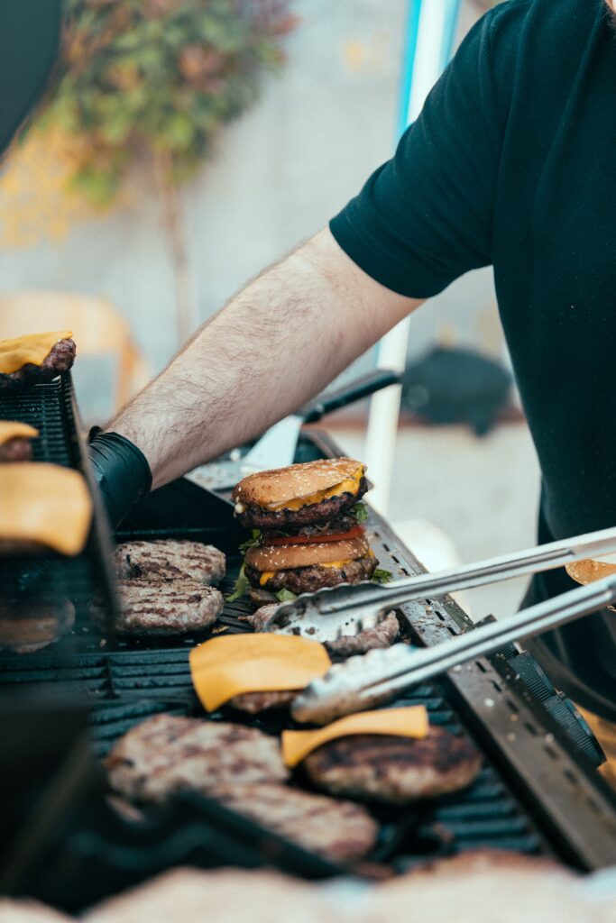 Person grilling juicy beef burgers with cheese on an outdoor barbecue.